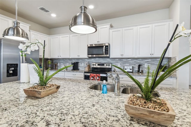 kitchen featuring decorative light fixtures, stainless steel appliances, light stone counters, and white cabinetry