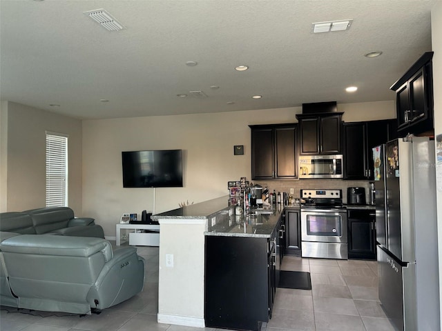 kitchen with light tile patterned flooring, light stone counters, kitchen peninsula, and appliances with stainless steel finishes