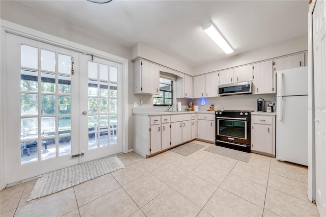 kitchen featuring light tile patterned floors, white fridge, black electric range oven, and white cabinetry