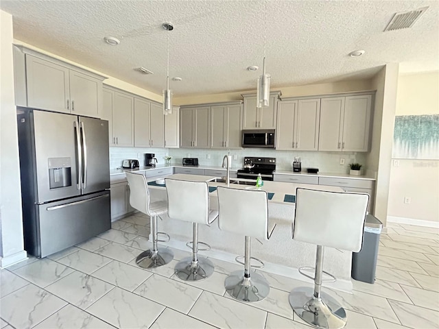 kitchen featuring appliances with stainless steel finishes, pendant lighting, gray cabinetry, a kitchen breakfast bar, and a kitchen island with sink