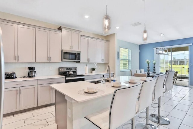 kitchen with gray cabinets, appliances with stainless steel finishes, pendant lighting, a kitchen breakfast bar, and a kitchen island with sink