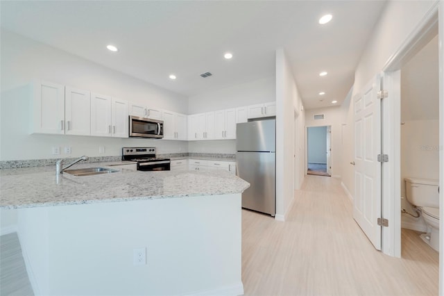 kitchen featuring white cabinetry, sink, light stone countertops, kitchen peninsula, and appliances with stainless steel finishes