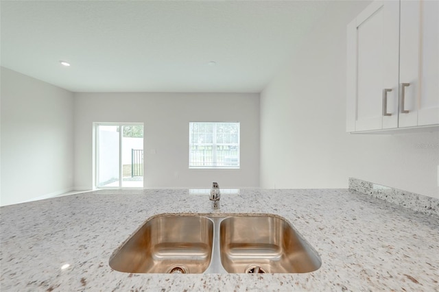 room details with white cabinetry, light stone countertops, and sink