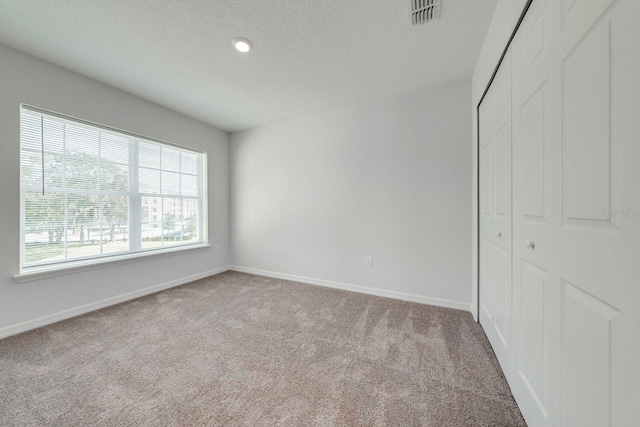 unfurnished bedroom featuring a textured ceiling, light colored carpet, and a closet