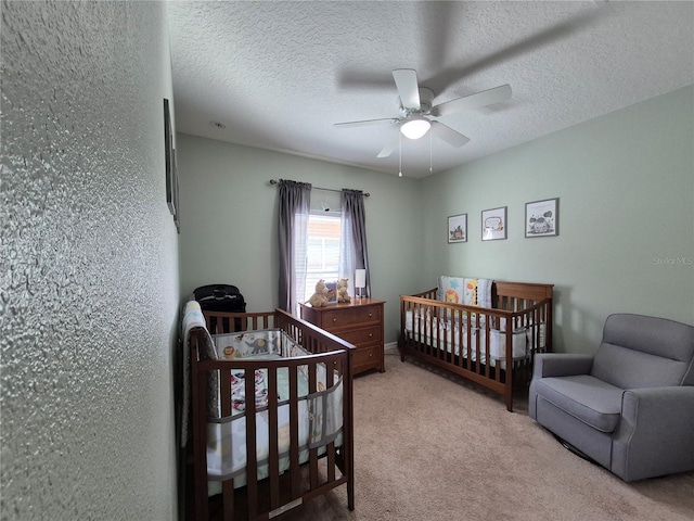 bedroom with a textured ceiling, a nursery area, light colored carpet, and ceiling fan