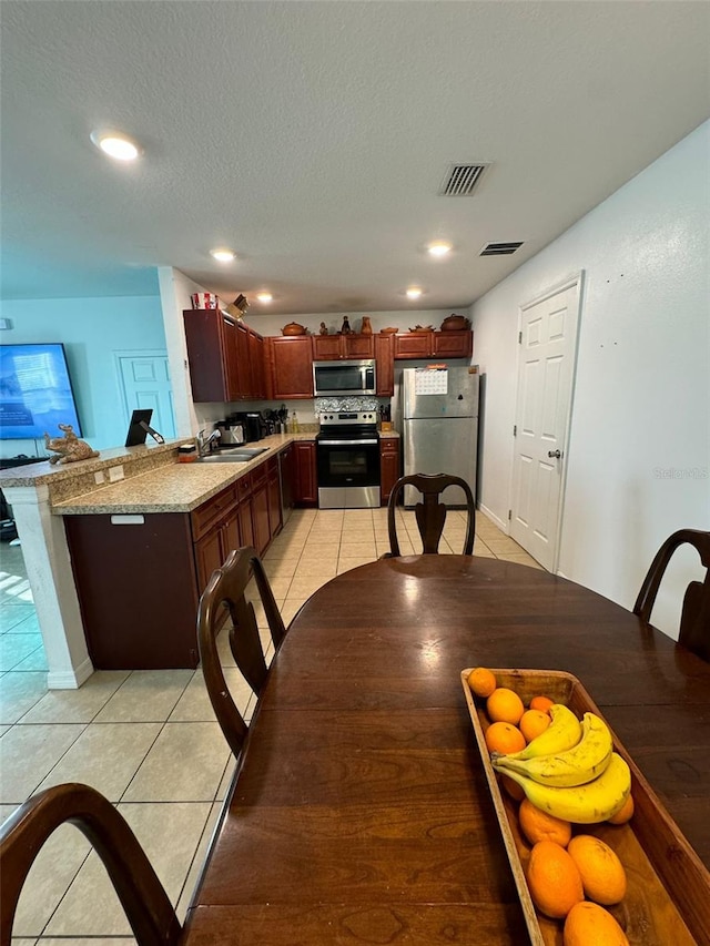 kitchen with a textured ceiling, light tile patterned flooring, light stone counters, kitchen peninsula, and stainless steel appliances