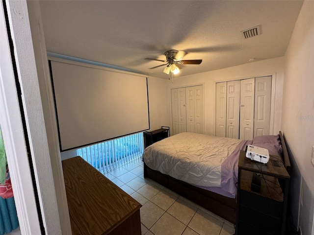 bedroom featuring multiple closets, ceiling fan, light tile patterned floors, and a textured ceiling