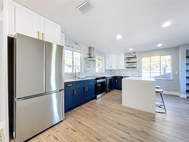 kitchen with appliances with stainless steel finishes, a kitchen breakfast bar, a center island, exhaust hood, and blue cabinetry