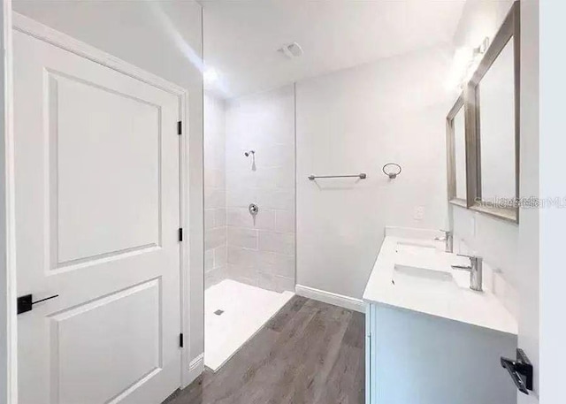 bathroom with a tile shower, vanity, and wood-type flooring