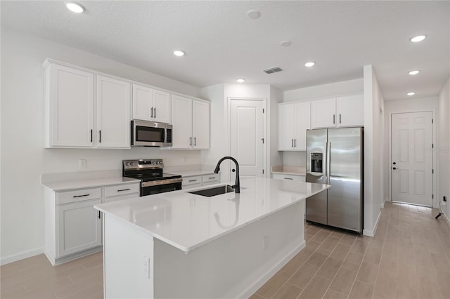 kitchen featuring white cabinets, sink, a textured ceiling, appliances with stainless steel finishes, and an island with sink