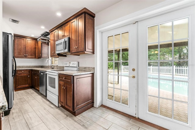 kitchen with a healthy amount of sunlight, light stone counters, sink, and appliances with stainless steel finishes