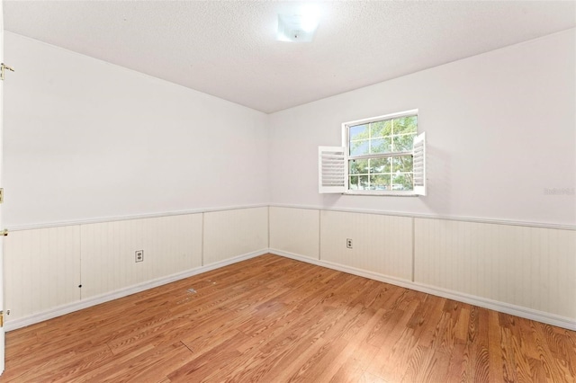 empty room with a textured ceiling and light hardwood / wood-style flooring