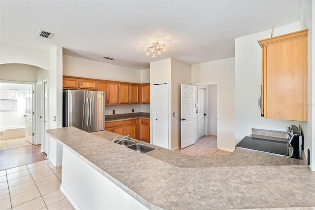 kitchen with light tile patterned flooring, range, sink, and stainless steel refrigerator