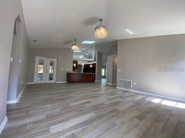 unfurnished living room featuring a chandelier, light hardwood / wood-style flooring, and vaulted ceiling with skylight