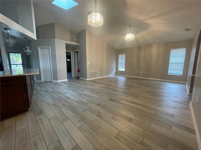 unfurnished living room featuring light wood-type flooring, a skylight, high vaulted ceiling, and a notable chandelier