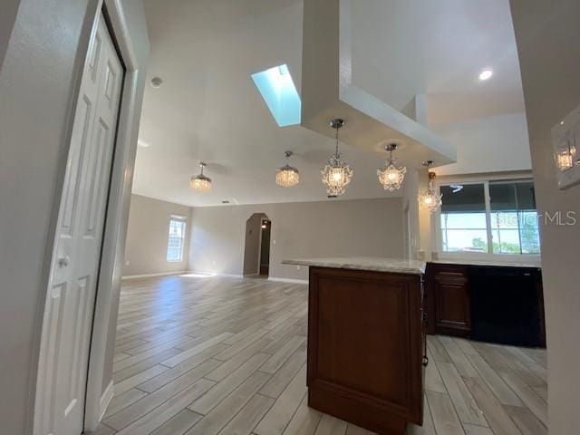 kitchen with pendant lighting, an inviting chandelier, a skylight, light hardwood / wood-style flooring, and a towering ceiling