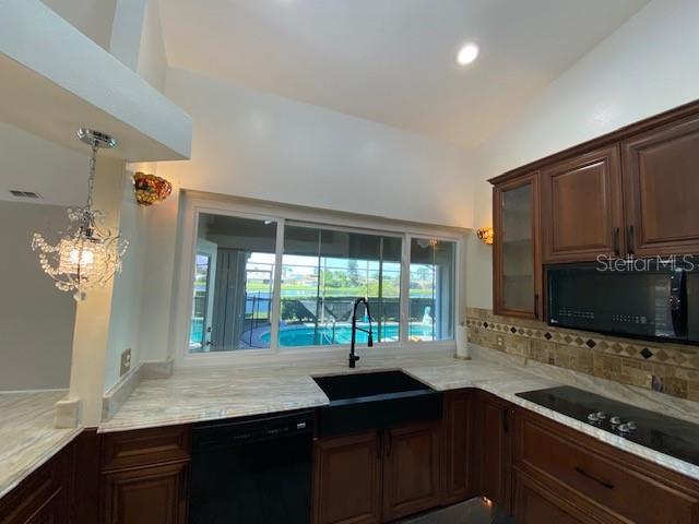 kitchen featuring light stone countertops, sink, a notable chandelier, backsplash, and black appliances