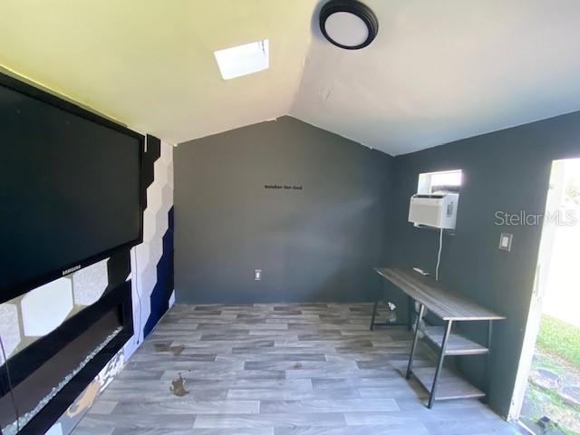 interior space featuring an AC wall unit, a wealth of natural light, vaulted ceiling with skylight, and hardwood / wood-style flooring