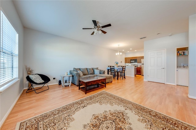 living room featuring ceiling fan with notable chandelier, washer / dryer, and light wood-type flooring