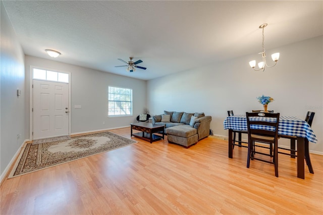 living room featuring ceiling fan with notable chandelier, light hardwood / wood-style floors, and a textured ceiling