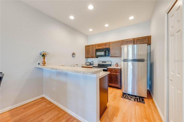 kitchen with kitchen peninsula, a kitchen breakfast bar, light wood-type flooring, and stainless steel appliances