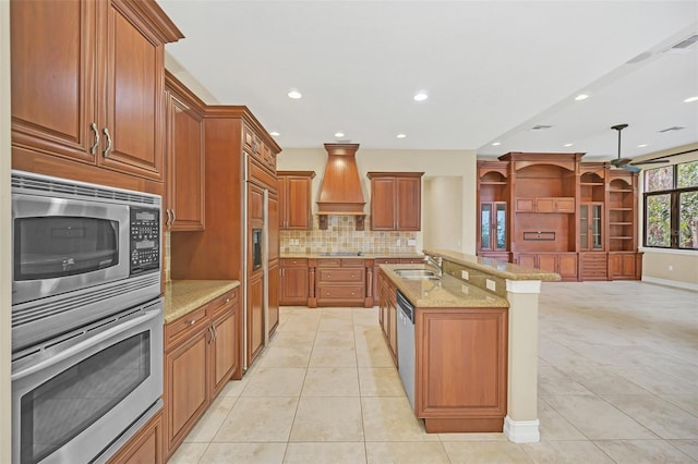 kitchen with light stone countertops, sink, stainless steel appliances, an island with sink, and light tile patterned floors