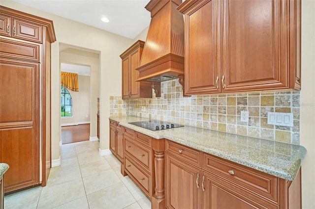 kitchen featuring tasteful backsplash, light stone counters, black electric stovetop, light tile patterned flooring, and custom exhaust hood