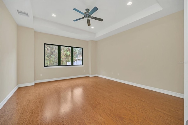 empty room featuring ceiling fan, light hardwood / wood-style floors, and a raised ceiling