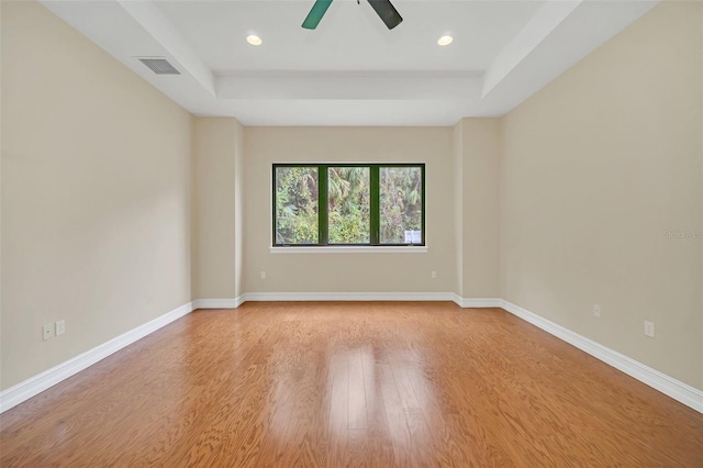 empty room with ceiling fan, light hardwood / wood-style floors, and a raised ceiling