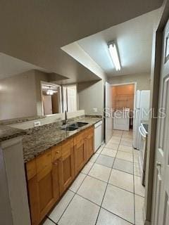 kitchen with dark stone countertops, sink, light tile patterned floors, and white fridge