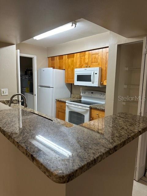 kitchen with white appliances, dark stone counters, and sink