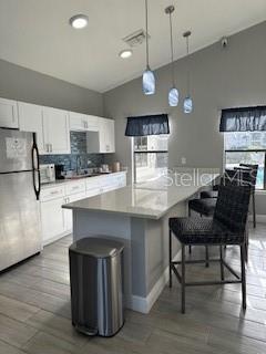 kitchen featuring white appliances, pendant lighting, a breakfast bar area, white cabinets, and lofted ceiling