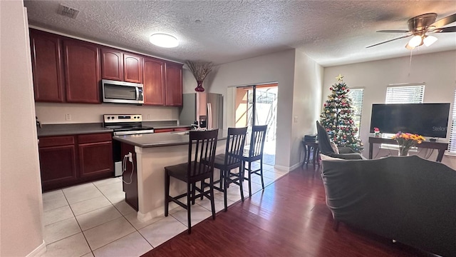 kitchen featuring a center island, light wood-type flooring, a textured ceiling, appliances with stainless steel finishes, and a kitchen bar