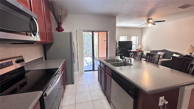 kitchen featuring ceiling fan, sink, an island with sink, a textured ceiling, and appliances with stainless steel finishes