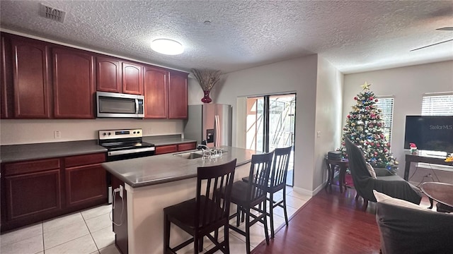 kitchen with sink, a textured ceiling, a center island with sink, appliances with stainless steel finishes, and light wood-type flooring