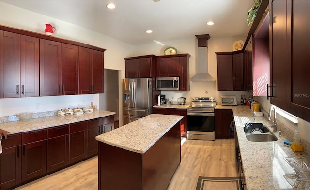 kitchen with appliances with stainless steel finishes, sink, a center island, wall chimney exhaust hood, and light stone countertops