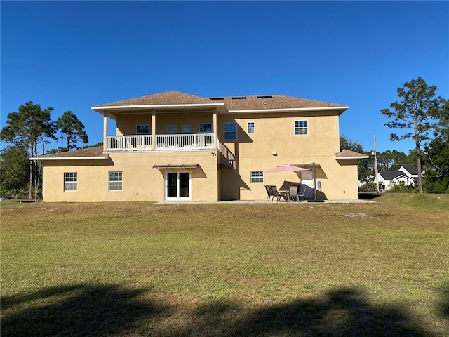 rear view of property featuring a patio, a yard, and a balcony