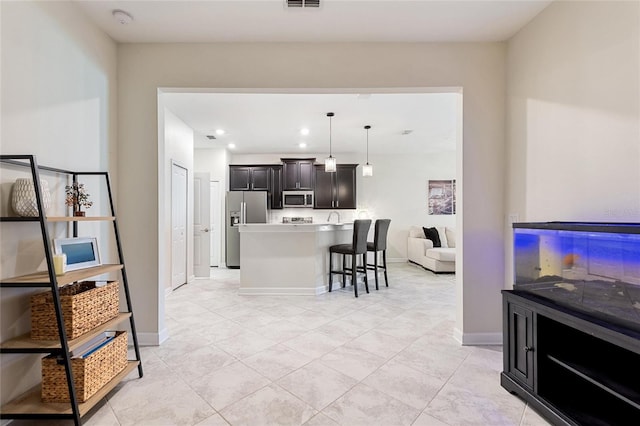 interior space featuring a breakfast bar, stainless steel appliances, decorative light fixtures, a center island, and light tile patterned flooring