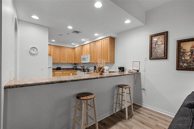 kitchen with white appliances, dark stone counters, a kitchen breakfast bar, light hardwood / wood-style flooring, and kitchen peninsula