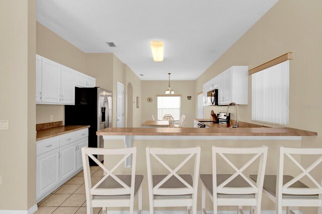 kitchen with a kitchen bar, light tile patterned floors, decorative light fixtures, and white cabinetry