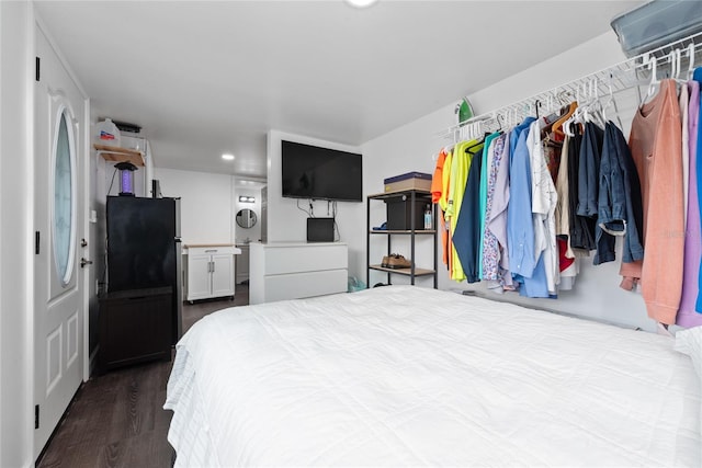 bedroom featuring hardwood / wood-style flooring, black refrigerator, and stacked washer / dryer