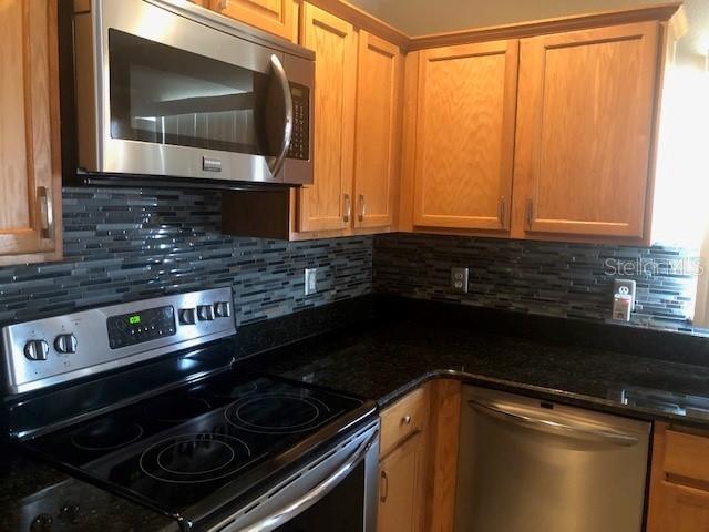 kitchen featuring dark stone countertops, decorative backsplash, and stainless steel appliances