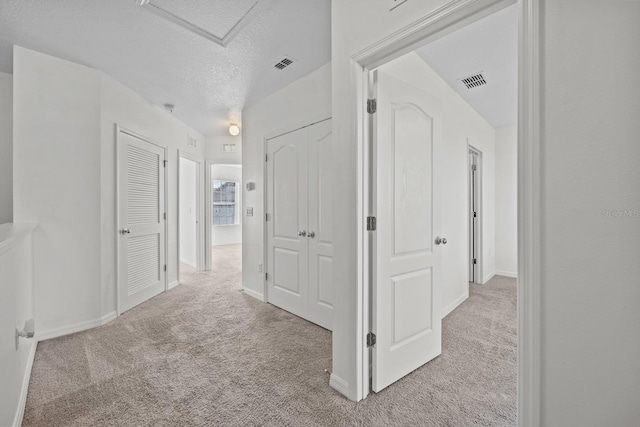 hallway with light carpet and a textured ceiling