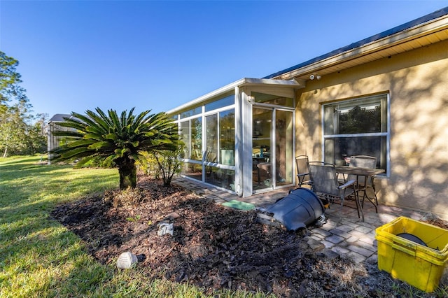 view of property exterior with a lawn, a sunroom, and a patio