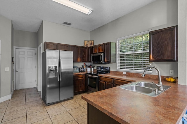 kitchen featuring dark brown cabinets, a textured ceiling, stainless steel appliances, sink, and light tile patterned flooring