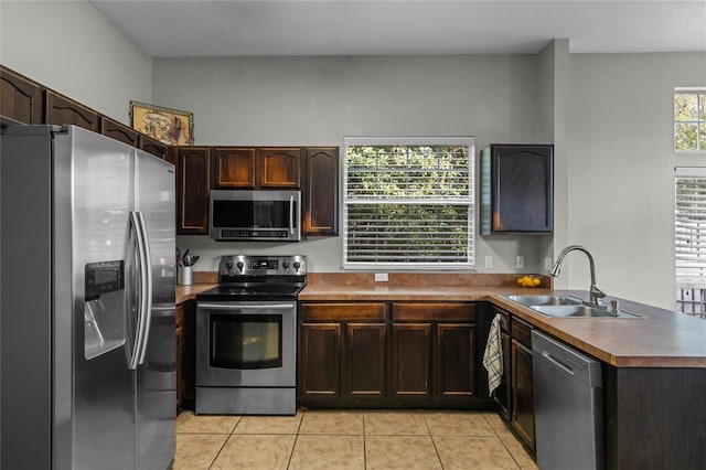 kitchen with sink, appliances with stainless steel finishes, dark brown cabinets, light tile patterned flooring, and kitchen peninsula