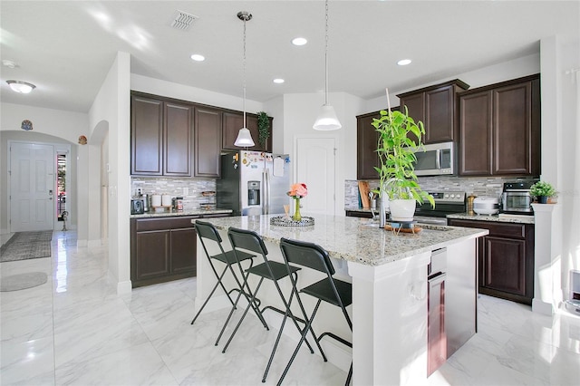 2811 Sonata Ct, Saint Cloud, FL 34772 - kitchen featuring appliances with stainless steel finishes, light marble finish flooring, arched walkways, decorative backsplash, and a kitchen island with sink