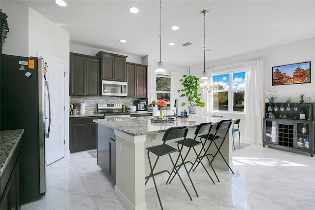 2811 Sonata Ct, Saint Cloud, FL 34772 - kitchen featuring appliances with stainless steel finishes, light marble finish floors, recessed lighting, an island with sink, and light stone counters