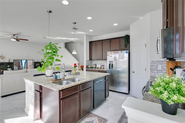 kitchen with appliances with stainless steel finishes, backsplash, sink, decorative light fixtures, and an island with sink