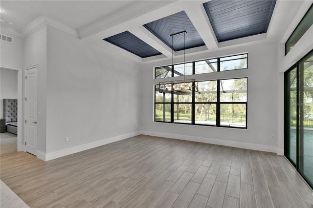 empty room featuring beamed ceiling, light hardwood / wood-style floors, and ornamental molding